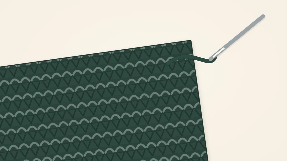 A tapestry needle threaded with a yarn tail resting on the corner of a knitted scarf