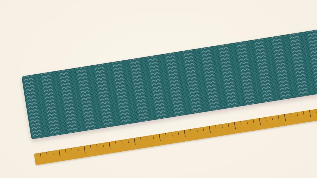 A long knitted scarf laid flat beside a tape measure